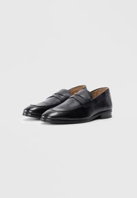 Mocassins en cuir noir à la finition lisse, avec un design cousu et un petit talon. L'intérieur est beige, contrastant avec l'extérieur noir.