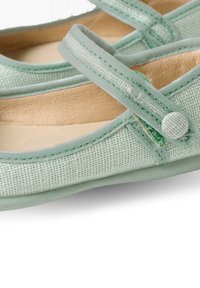 Hellgrüne Stoffballetschuhe mit strukturiertem Obermaterial, flacher Sohle und einem Riemen mit einer Knopfakzent.