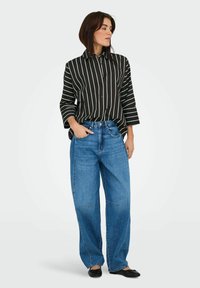 Zwart-wit gestreepte button-up shirt met lange mouwen, gecombineerd met lichtblauwe brede denim jeans en zwarte platte schoenen.