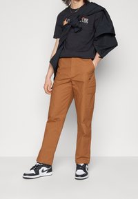 Svart bomull T-shirt med logotyp, bruna cargobyxor med sidofickor och svartvita hög- topp sneakers. Avslappnad outfit.