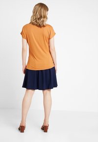Top arancione a maniche corte abbinato a una gonna svasata blu navy. Il tessuto è liscio e leggero, con sandali con tacco marroni come calzature.