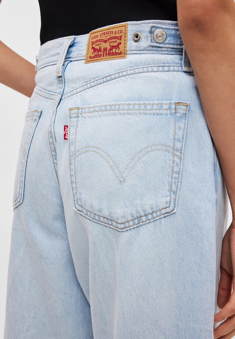 Lyseblå denimjeans med høj talje, der har en brun læderpatch fra Levi's, en rød fane på baglommen og baglommer med buede syninger.