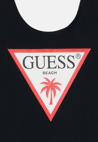 Fekete trikó, amelyen egy nagy fehér háromszög piros kerettel található. Az elülső részen a "GUESS" felirat feketével, alatt pedig a "BEACH" felirat található, mellette egy piros pálmafa.