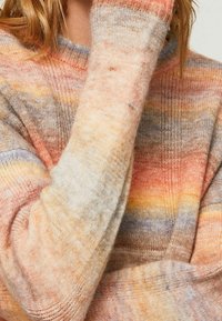 Pull tricoté multicolore en laine douce, présentant des teintes pastel d'orange, jaune et gris avec une coupe décontractée et des poignets côtelés.