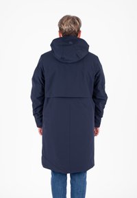 Cappotto impermeabile navy con cappuccio, caratterizzato da una silhouette ampia, maniche lunghe e uno spacco sul retro per la ventilazione. Texture liscia, design minimale.