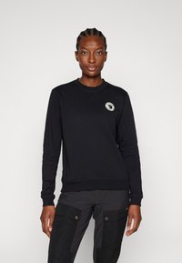 Felpa nera con colletto rotondo, polsini e orlo a costine, caratterizzata da un'appliqué circolare con logo sul petto. Tessuto liscio, vestibilità casual.
