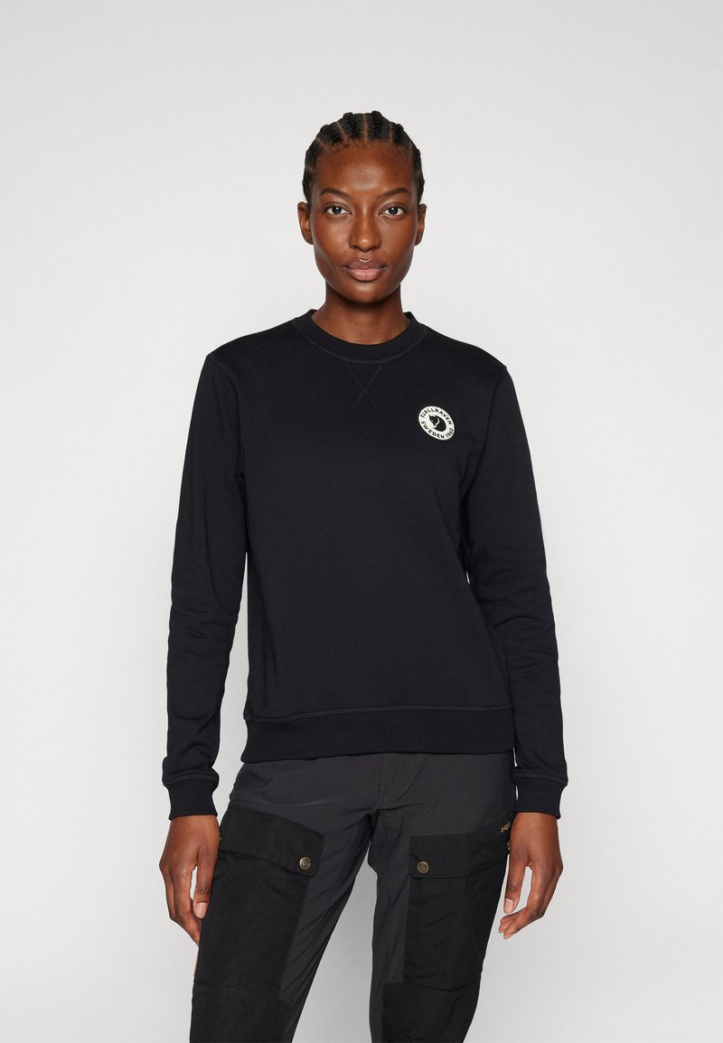 Felpa nera con colletto rotondo, polsini e orlo a costine, caratterizzata da un'appliqué circolare con logo sul petto. Tessuto liscio, vestibilità casual.