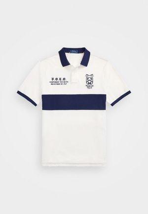 Biely polo tričko s námorníckym modrým vodorovným pruhom, vyšívaným logom a textovým detailom na ľavej strane; klasický golier a krátke rukávy.