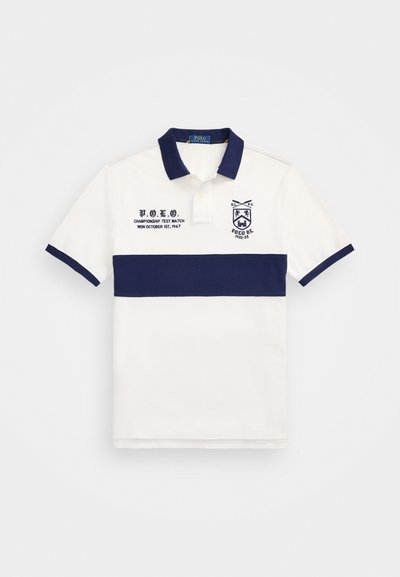 Balta polo krekls ar tumši zilu horizontālu svītru, izšūtu logo un tekstu uz kreisās puses; klasiskā apkakle un īsas piedurknes.