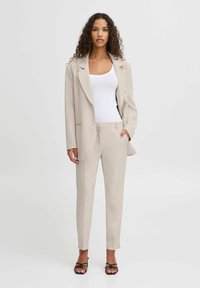 Beige přizpůsobený blazer s jedním knoflíkem, doplněný o úzké kalhoty ve stejném odstínu. Vyznačuje se hladkým, jemným materiálem a minimalistickým designem.