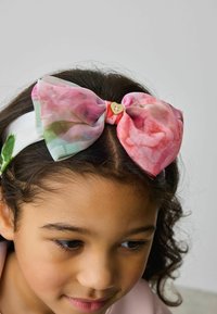Fascia per capelli con motivi floreali e un grande fiocco rosa, realizzata in tessuto trasparente, con un accento a forma di cuore dorato al centro.
