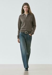 Bruine wollen trui met kraag, gecombineerd met losse blauwe spijkerbroek. Zwarte riem en schoenen completeren de look. Eenvoudig, strak ontwerp.