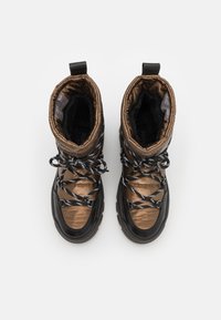 Brune og sorte vinterstøvler med kviltet overdel, struktureret krave og snørebånd med sort-hvide mønstre. Gummisål med markant skridbane.