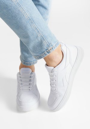 Białe buty sportowe z gładką skórzaną powierzchnią, zaokrąglonym noskiem i perforowanymi detalami na przodze; zestawione z jasnoniebieskim dżinsem.