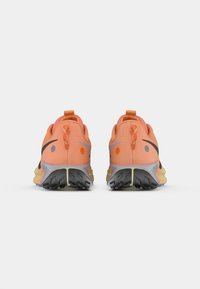 Chaussures de sport avec un dessus en mesh orange, accents noirs et une semelle grise texturée présentant des crampons profonds pour une meilleure adhérence. Une languette à l'arrière est particulièrement remarquable.
