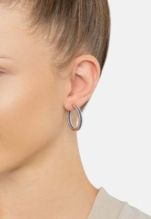 Gold-tone metal hoop earrings featuring a blue crystal accent, displaying a textured finish and circular shape, worn on an ear.