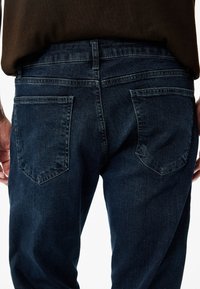 Tumman pesun farkut, joissa on slim fit -leikkaus ja kaksi takataskua. Kankaalla on sileä pinta ja vähäinen haalistuminen, sekä kontrastiväriset ompeleet.