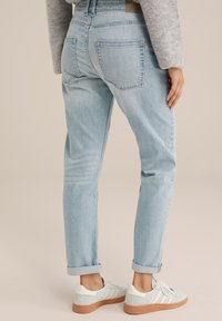 Ljust blå denimjeans med tapered passform, upprullade benslut och två bakfickor, tillsammans med ljusa sneakers med gummisula.