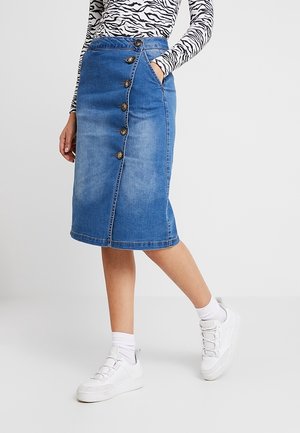Denim skirt in light blue with front button detail, knee-length cut, subtle fading, and a back slit. Paired with white sneakers and socks.
