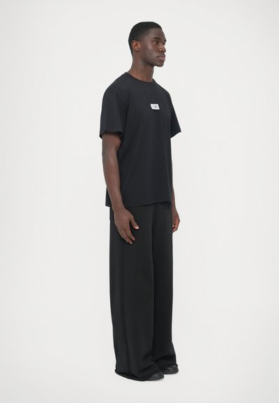 Μαύρο βαμβακερό μπλουζάκι με ίσια γραμμή και κοντά μανίκια, με μια μικρή ετικέτα εμπρός. Συνδυασμ�ένο με μαύρο φαρδύ παντελόνι.