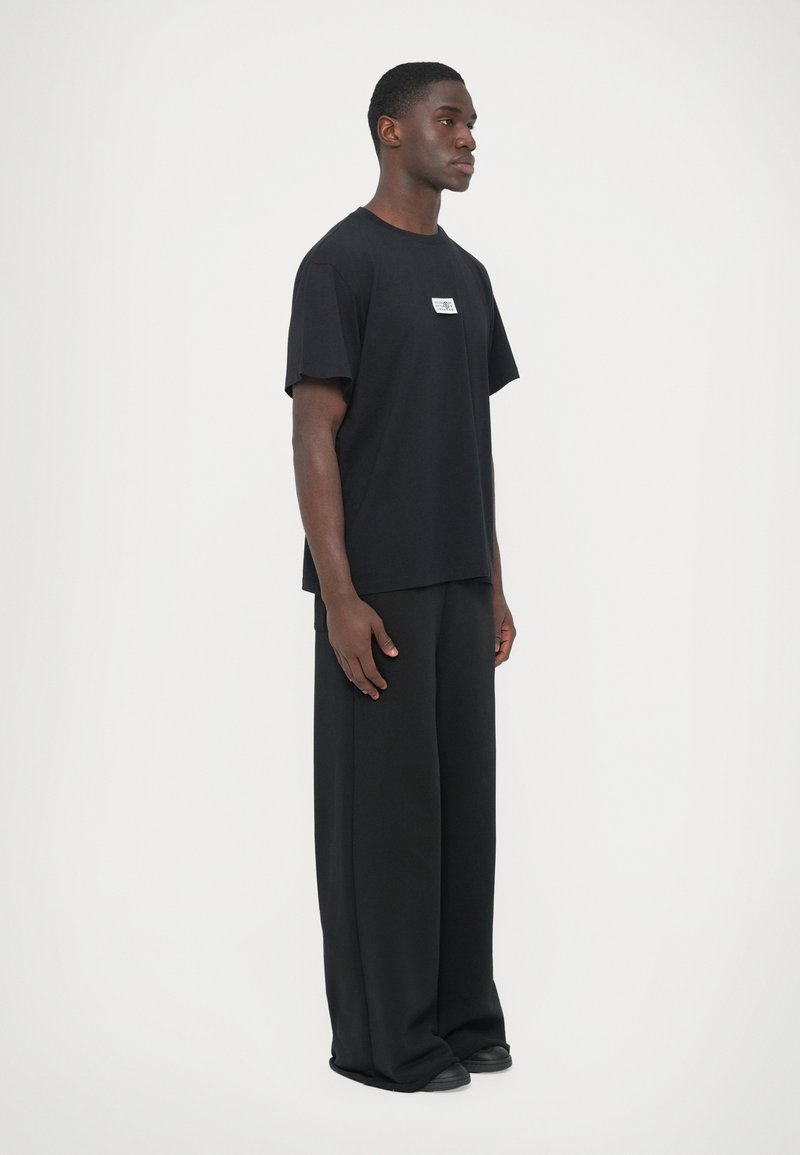 Sort bomuld t-shirt med lige snit og korte ærmer, med en lille label foran. Kombineret med løstsiddende sorte bukser.