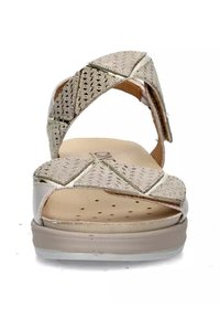 Sandali beige con tomaia metallizzata testurizzata, fascette incrociate e suola imbottita. Suola intermedia chiara e dettagli decorativi.