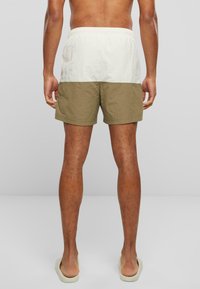 Shorts de bain pour homme avec un design coloré en crème clair et vert olive, taille élastique et texture lisse. Longueur courte.