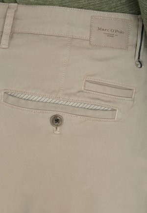 Beige Baumwollhosen mit einem Knopf, Gesäßtasche und einem Etikett mit der Aufschrift "Marc O'Polo." Die Tasche hat einen blauen Akzent am Taschenöffnung.