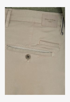 Beige Baumwollhosen mit einem Knopf, Gesäßtasche und einem Etikett mit der Aufschrift "Marc O'Polo." Die Tasche hat einen blauen Akzent am Taschenöffnung.