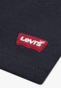 Tissu noir à texture côtelée, comportant une étiquette avec le logo Levi's rouge cousue sur un côté. Le design est simple et épuré.