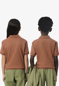 Due bambini indossano polo a maniche corte di colore marrone con un tessuto strutturato, abbinate a pantaloni cargo di colore verde chiaro.
