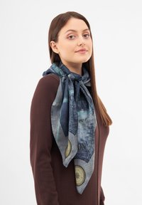 Pañuelo de seda con un diseño de mapa de ciudad en azul y gris, con acentos de brújula circular, atado alrededor del cuello.