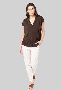 Haut marron à manches courtes avec un décolleté en V, associé à un pantalon blanc et des sandales à brides marron. Tissu lisse avec une coupe décontractée.