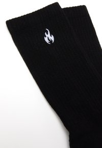 Calcetines de canalé negros hechos de una tela suave, con un logo de llama bordado en blanco en el costado.