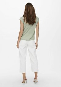 Top de manga corta color verde claro con un ajuste ligeramente holgado, combinado con pantalones anchos blancos y sandalias de tacón transparente. Diseño simple.