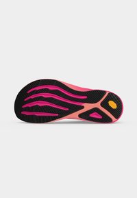 Semelle de chaussure avec une bande de roulement noire et des rainures roses, affichant un logo hexagonal jaune près du talon sur un fond gris clair uni.