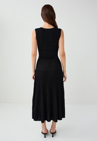 Schwarzes geripptes Strickkleid mit tailliertem Oberteil und einem gefalteten, fließenden Rock. Ärmelloses Design mit rundem Ausschnitt und knöchellanger Länge.