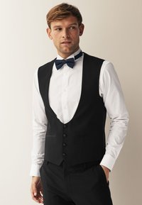 Chaleco formal negro con escote en V profundo, seis botones y corte Slim Fit, combinado con una camisa blanca y una pajarita azul marino, que destaca por su tejido suave y líneas limpias.