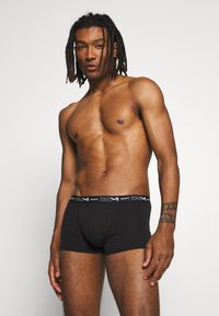 Schwarze Baumwoll-Boxershorts mit einem kontrastierenden schwarzen Bund, der das "DIM"-Logo trägt. Glatte Textur, enganliegendes Design und Länge bis zur Mitte des Oberschenkels.