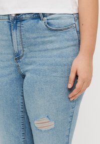 Light blue denim jeans with a distressed knee area. Features a classic five-pocket design and silver hardware at the waist.