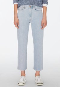 Světlomodré džíny s rovný střih, surovým lemem a designem s pěti kapsami, doplněné bílými teniskami s černými akcenty.