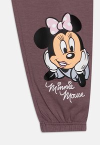 Fialové legíny s grafikou Minnie Mouse, která má na hlavě růžovou puntíkovanou mašli, bílé rukavice a nápis "Minnie Mouse" ve zlatém písmu.