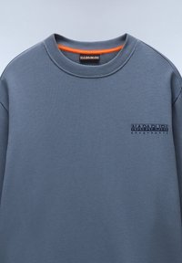 Gray sweatshirt with a crew neckline. Features a small navy blue logo on the left chest. Soft texture and relaxed fit. Orange accent interior.