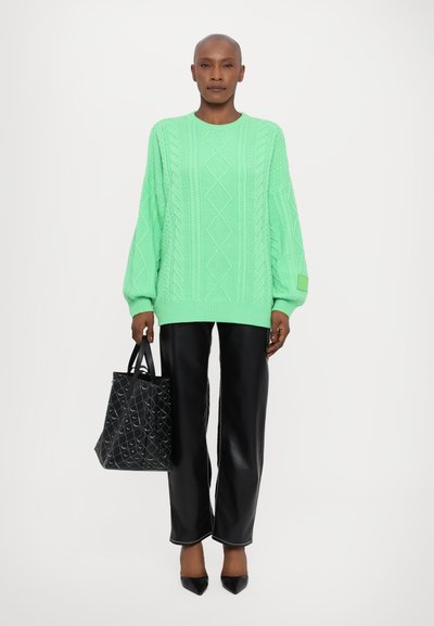 Maglione a coste verde menta con maniche oversize, abbinato a pantaloni in ecopelle neri e a una borsa a tracolla nera a fantasia. Décolleté nere a punta.