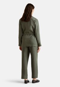 Conjunto de lino ligero en verde oliva, que incluye una blusa de manga larga y pantalones rectos. La blusa tiene un corte relajado y detalles de botón en los puños.