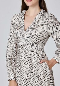 Robe à manches longues en tissu crème avec des lignes abstraites noires, avec un décolleté en V, une taille froncée et des poches latérales. Finition texturée.
