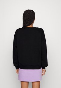 Felpa nera con maniche lunghe e orlo a coste, abbinata a una gonna viola chiaro. La texture appare liscia, creando un look casual.