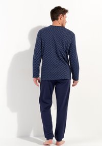 Marineblå to-delt pyjamasæt med langærmet bluse, der har et geometrisk mønster, og løstsiddende ensfarvede bukser. 100% bomuldsstof, blød tekstur.