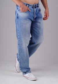 Hellblaue Denim-Jeans mit einem ausgewaschenen Finish, geradem Bein und Fünf-Taschen-Design. Kombiniert mit weißen Turnschuhen mit roten Akzenten.