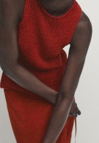 Haut rouge en maille avec un col rond et un motif texturé, assorti à une jupe rouge. Le tissu semble respirant et éclatant.